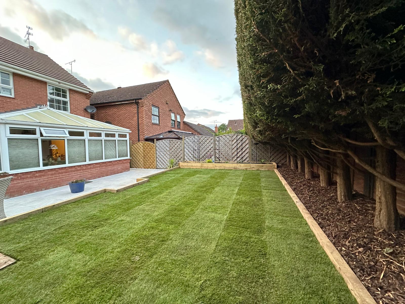 Striped lawn with patio and conservatory at dusk