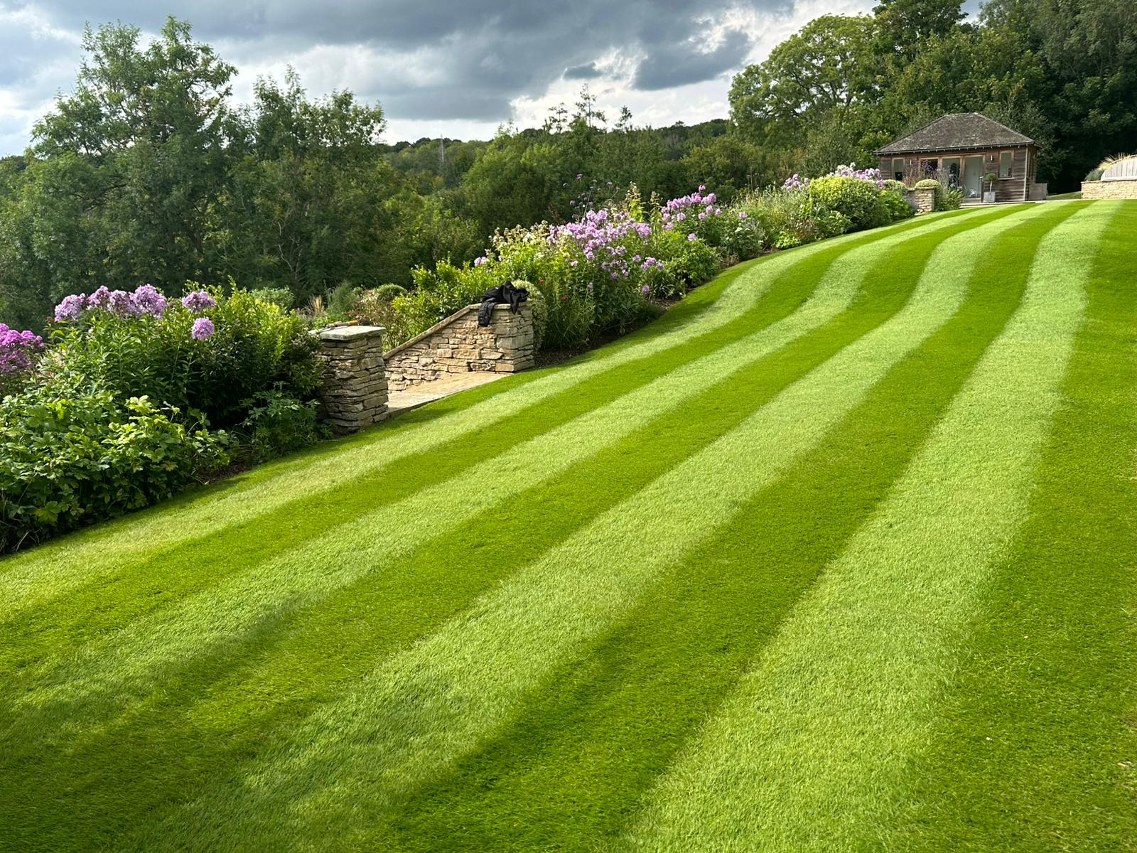 Striped lawn with stone wall and summer house